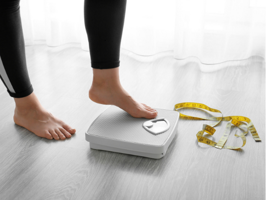 Women stepping on a scale with a tape measure next to it